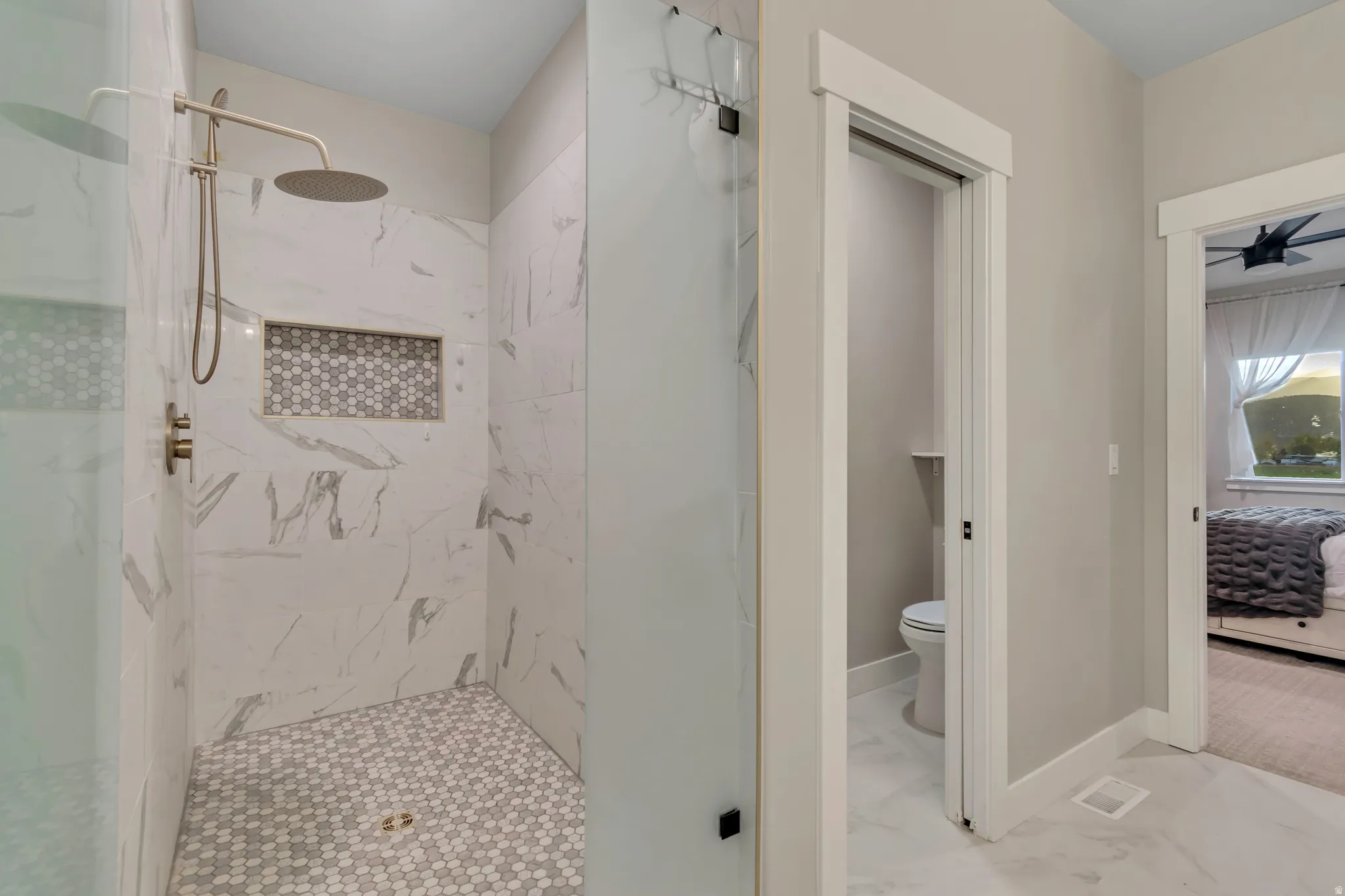 Spacious walk-in shower featuring large format wall tile, hexagonal floor tile, a tiled niche, and a rain shower head with gold-finish fixtures