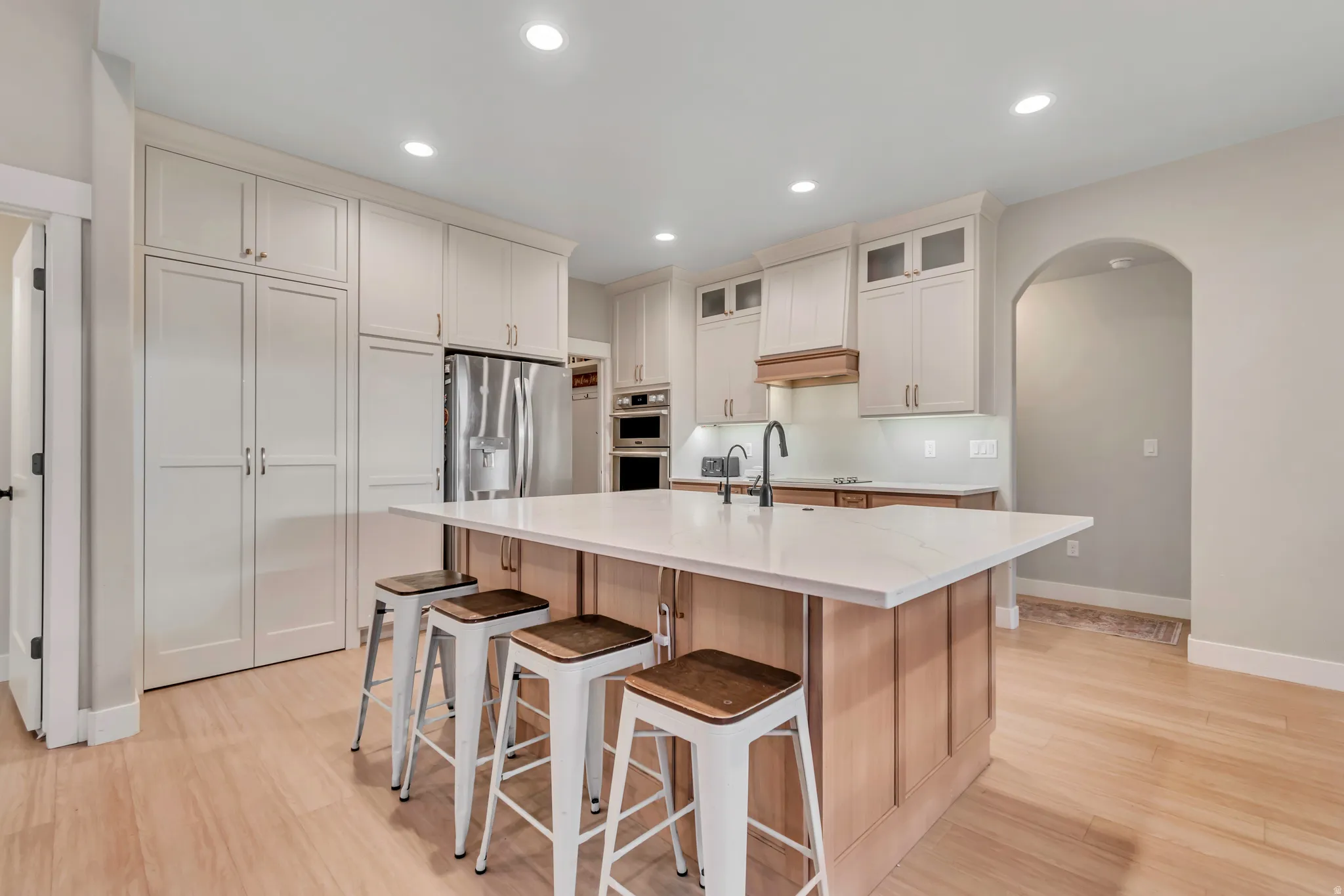 Contemporary kitchen featuring a large central island with a white countertop, light wood cabinetry, recessed lighting, and stainless steel appliances