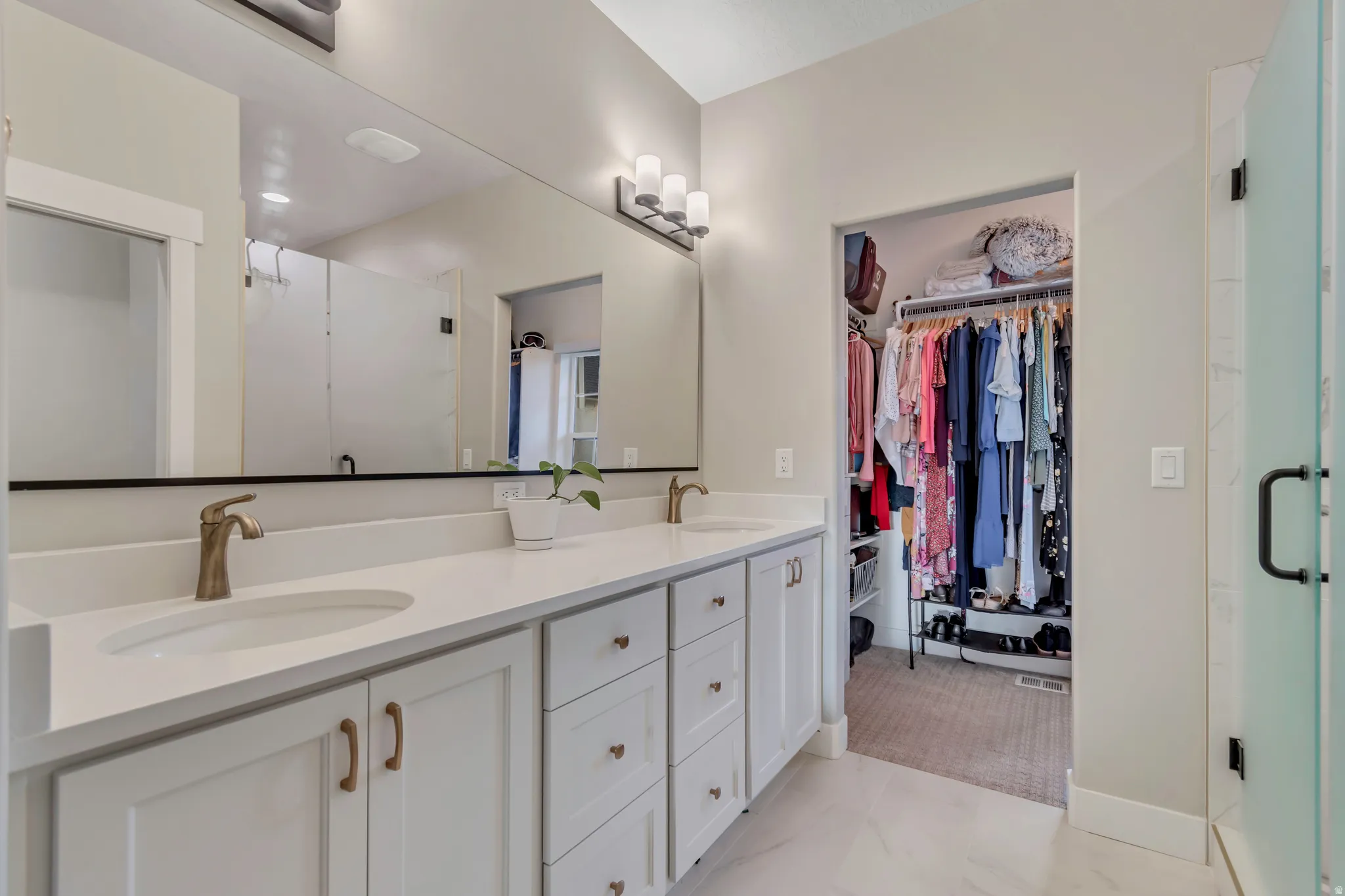 Bathroom featuring a double vanity with white cabinetry, light-toned countertops, and brushed brass fixtures