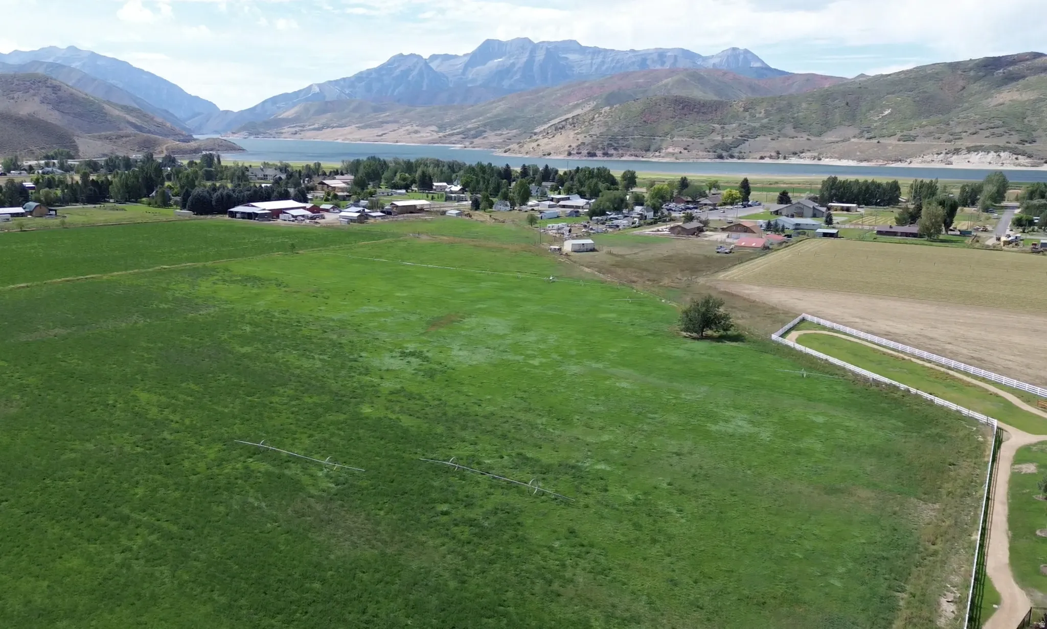 Expansive green fields with distant mountainous terrain, a body of water, and residential structures