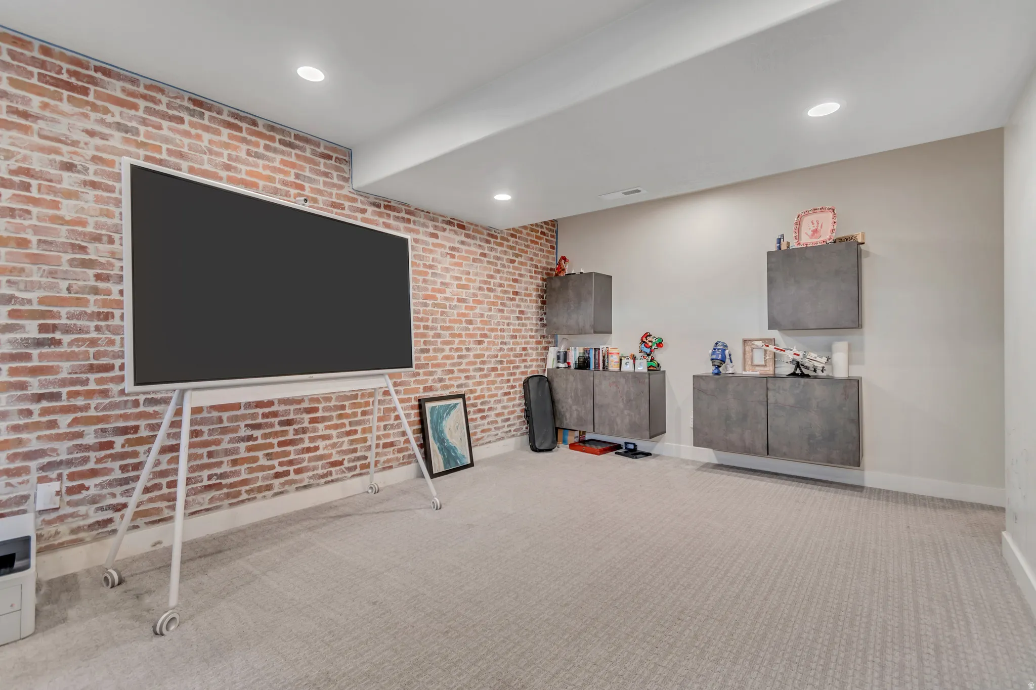 Exposed brick accent wall with recessed lighting, complemented by light-toned wall-to-wall carpeting and floating cabinetry