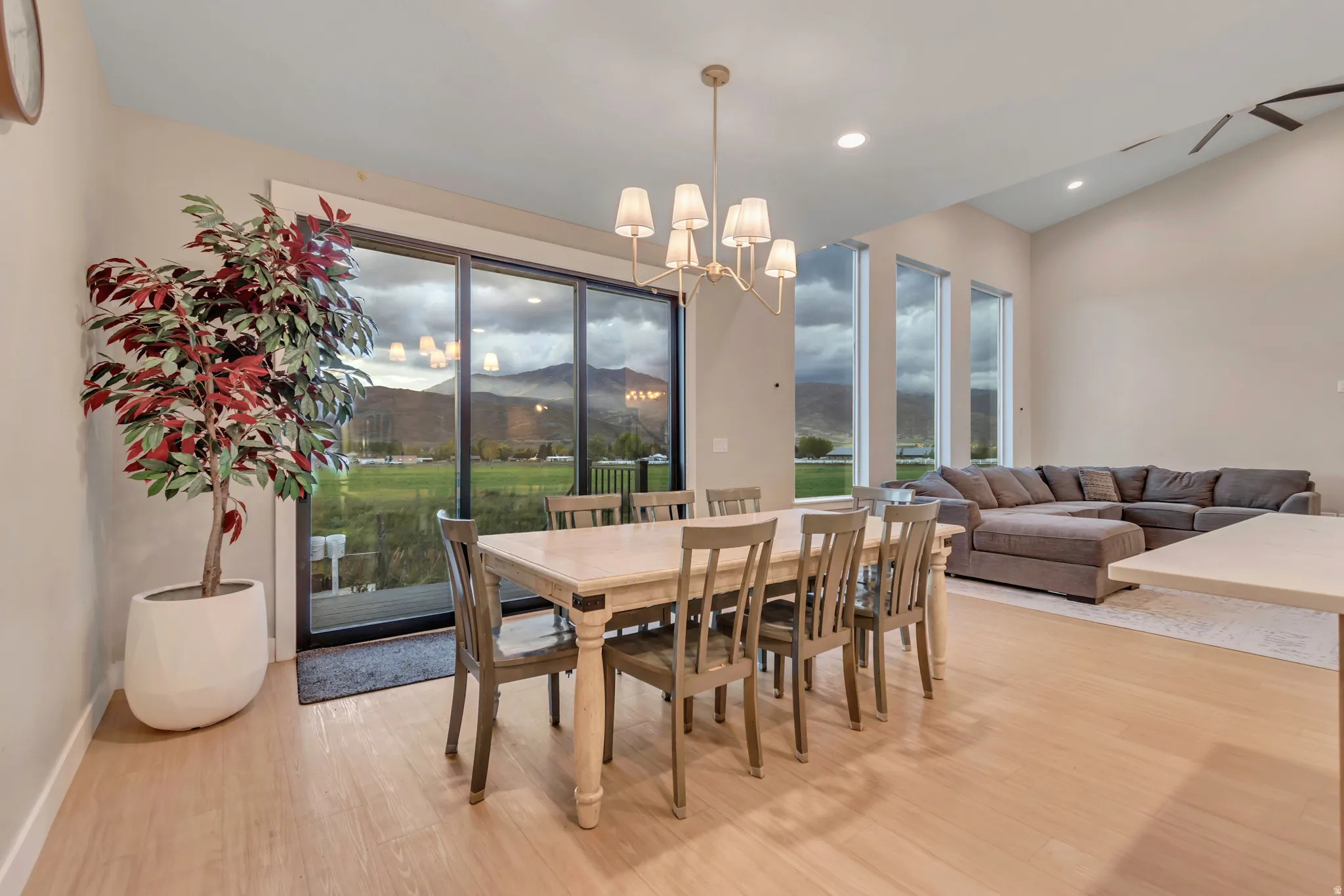 Open-concept living area featuring light wood-finish flooring, a contemporary chandelier, multiple vertical windows, recessed lighting, and a vaulted ceiling