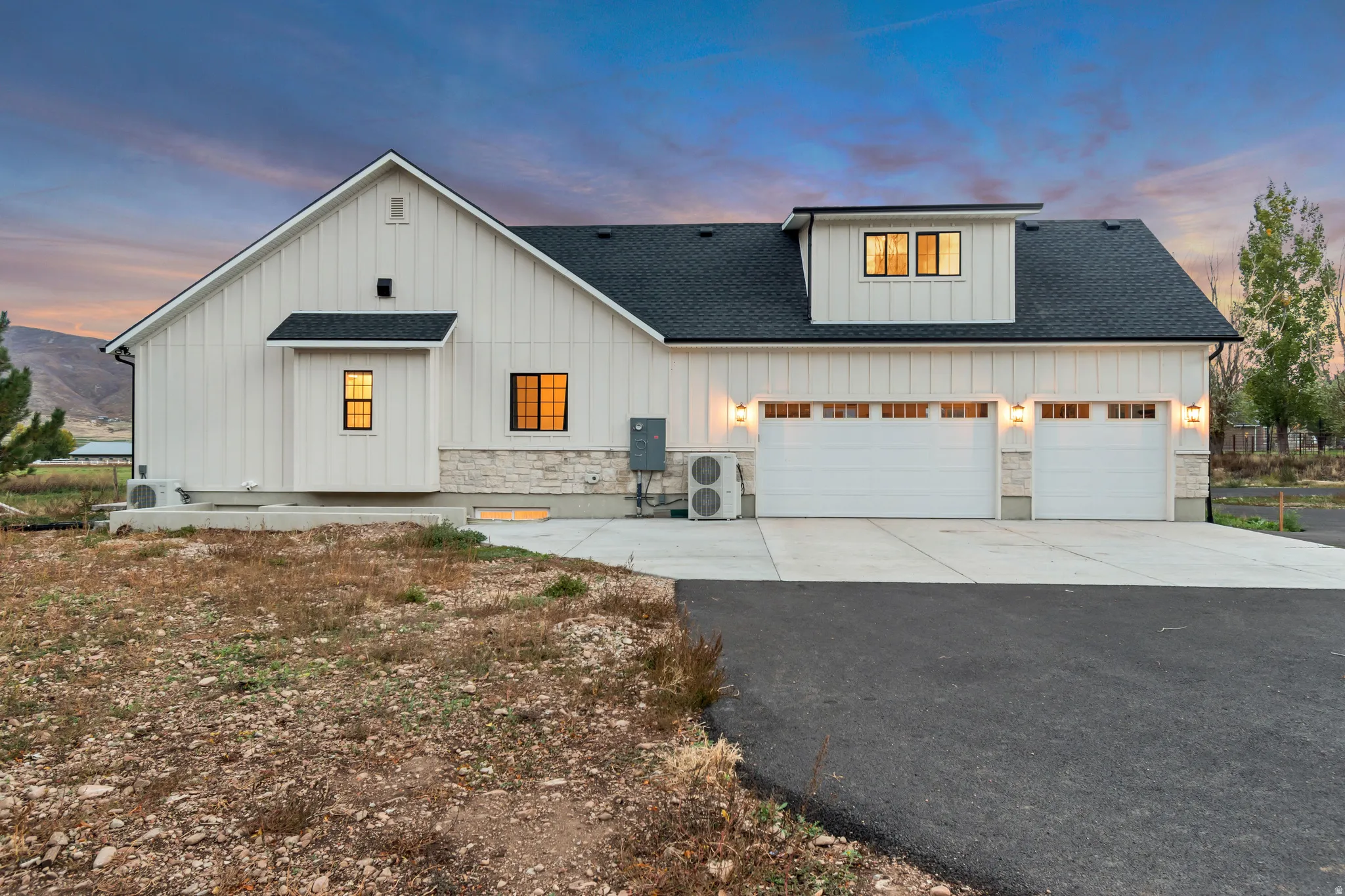 Modern farmhouse exterior featuring vertical board and batten siding, stone accents, a dark asphalt shingle roof, and a prominent dormer with multiple windows