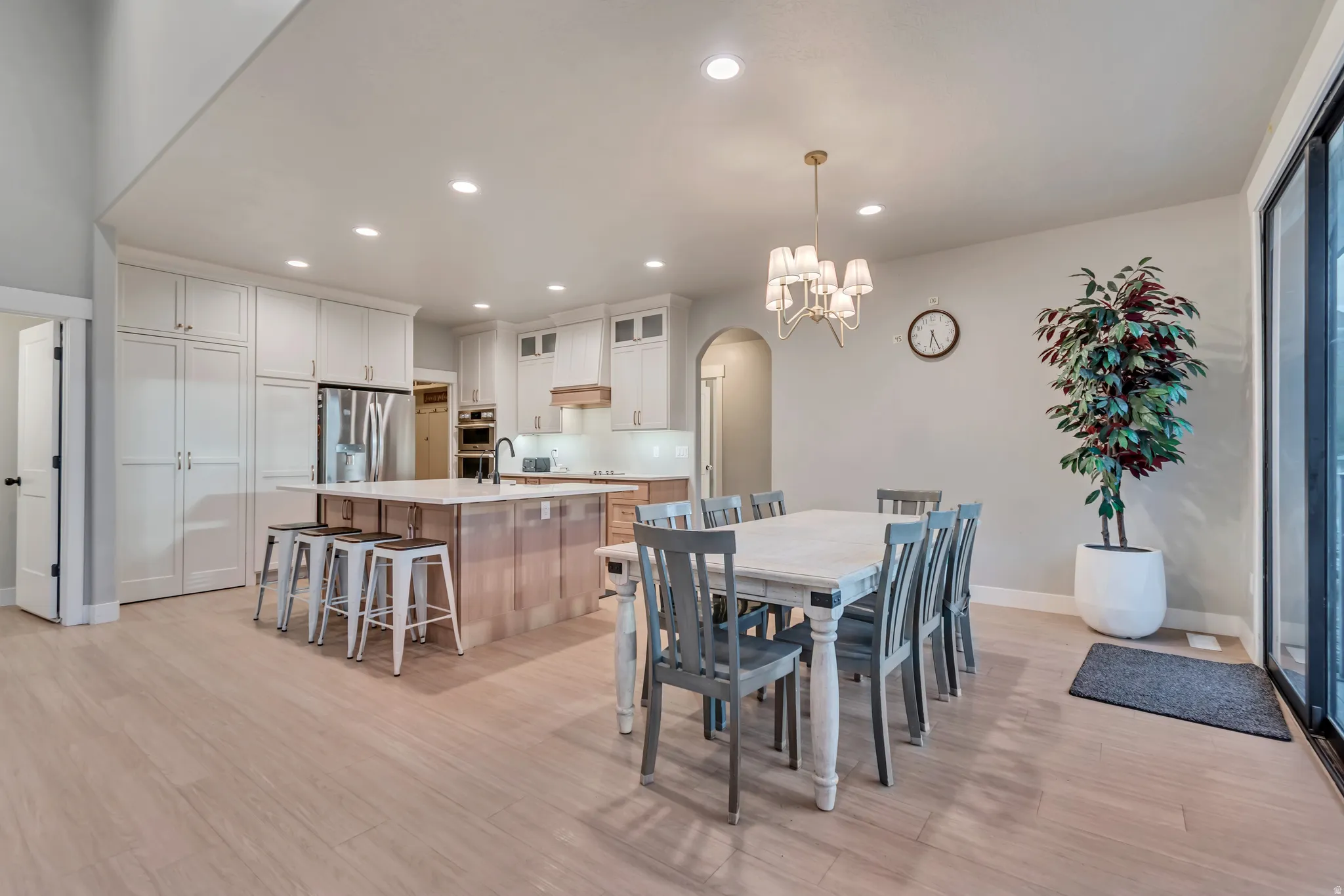 Open-concept kitchen and dining area featuring light wood-finish flooring, a kitchen island with seating, white shaker-style cabinetry, stainless steel appliances, and recessed lighting