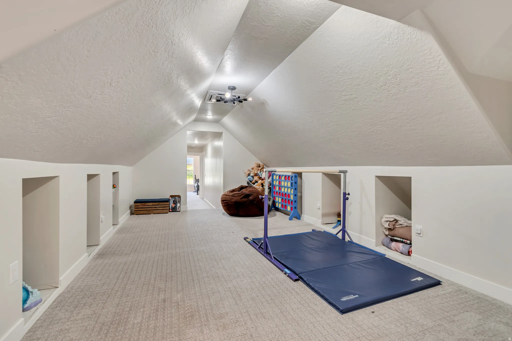 Spacious attic space featuring a textured ceiling, recessed lighting, neutral carpeting, multiple built-in storage nooks, and a contemporary ceiling light fixture