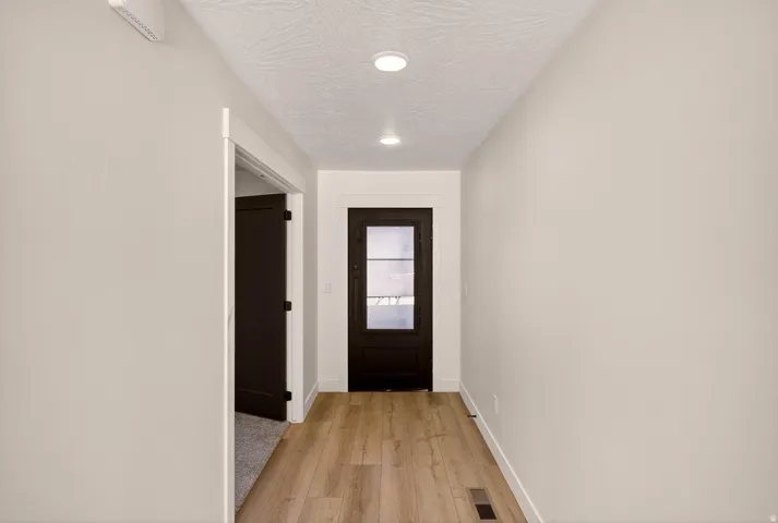 Hallway featuring wood-finish flooring, recessed lighting, and a dark-paneled door with frosted glass