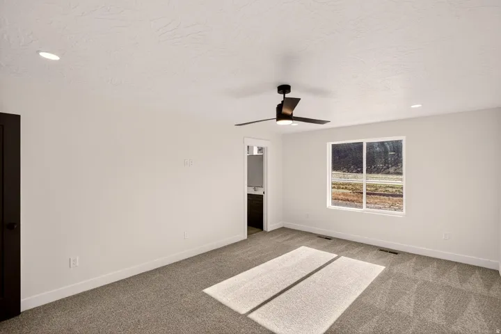 Spacious room featuring neutral carpeting, a modern ceiling fan with integrated lighting, and a large window