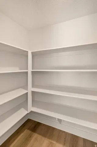 Corner pantry featuring extensive white shelving and wood-finish flooring