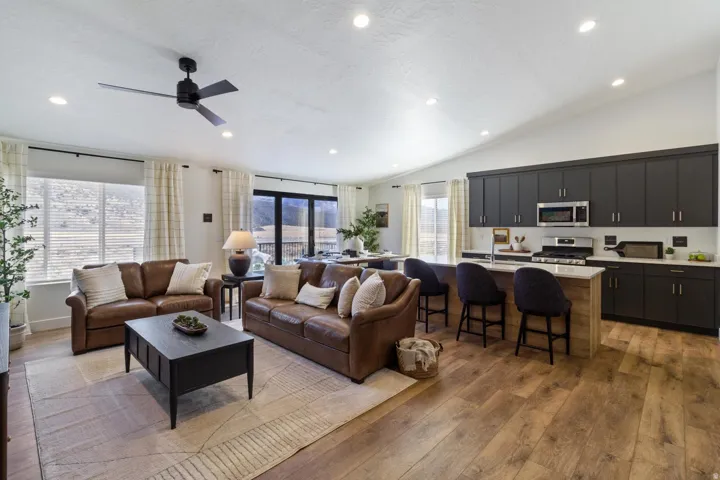 Open-concept living space featuring wood-finish flooring, recessed lighting, a vaulted ceiling, and dark cabinetry with stainless steel appliances