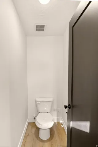 Dedicated water closet with wood-finish flooring, a white toilet, recessed ceiling light, and a dark-paneled door with matte black hardware