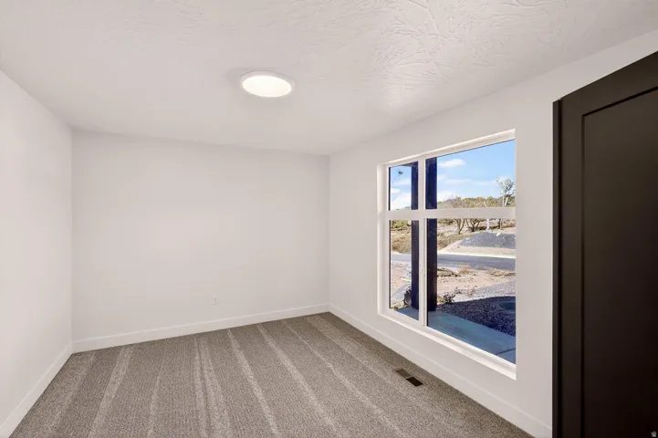 Bright interior room featuring a large window, textured white walls, recessed ceiling lighting, gray patterned carpet, and a dark paneled door