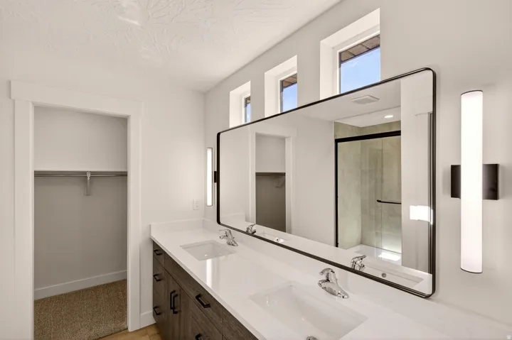 Bathroom featuring a double vanity with stone countertops and wood-finish cabinetry, a large frameless mirror, and modern vertical wall sconces