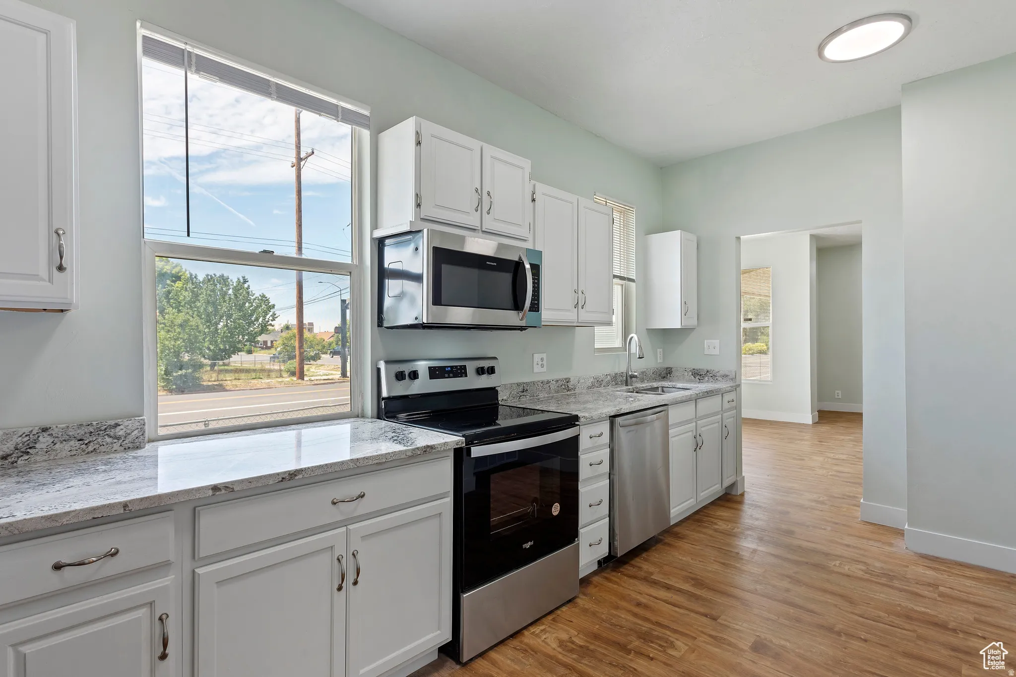 Kitchen featuring white cabinetry, stainless steel appliances, granite countertops, and wood-finish flooring