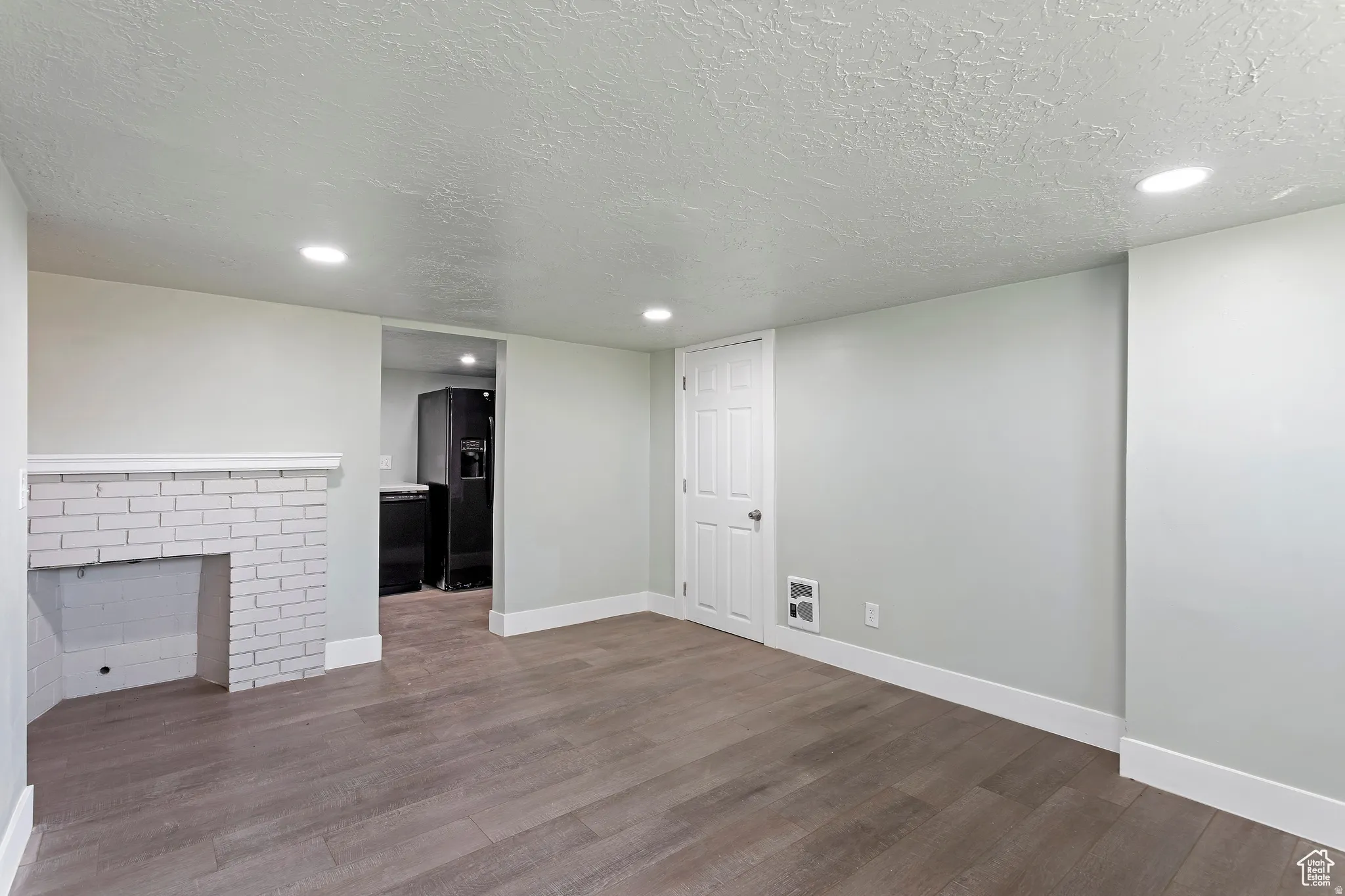 Spacious room featuring wood-finish flooring, a white brick fireplace, recessed lighting, and a white paneled door