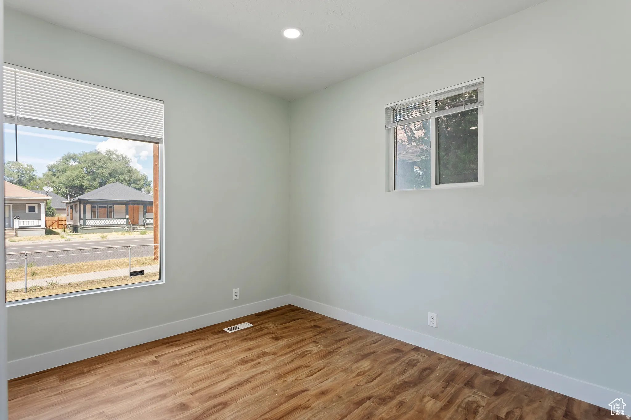 Room featuring two windows with white trim, wood-finish flooring, and light-colored walls