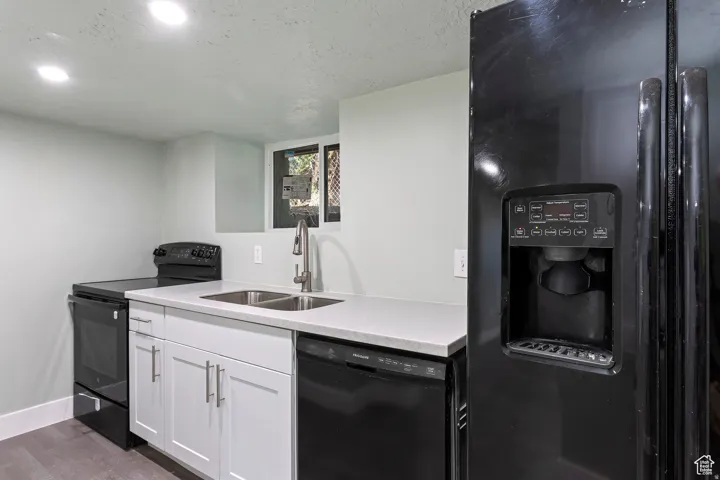 Modern kitchen featuring a black refrigerator with ice and water dispenser, stainless steel sink with gooseneck faucet, white shaker-style cabinetry, and light-toned countertops