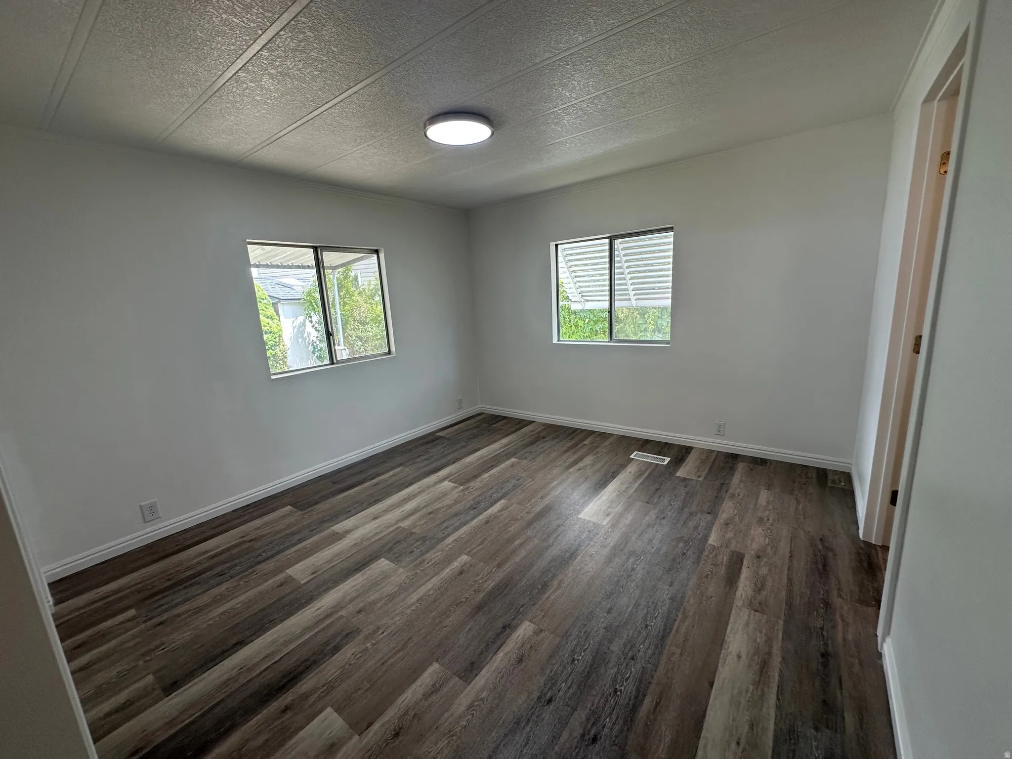 Interior room featuring wood-finish flooring, two window openings with horizontal blinds, white baseboards, and a flush-mount ceiling light fixture