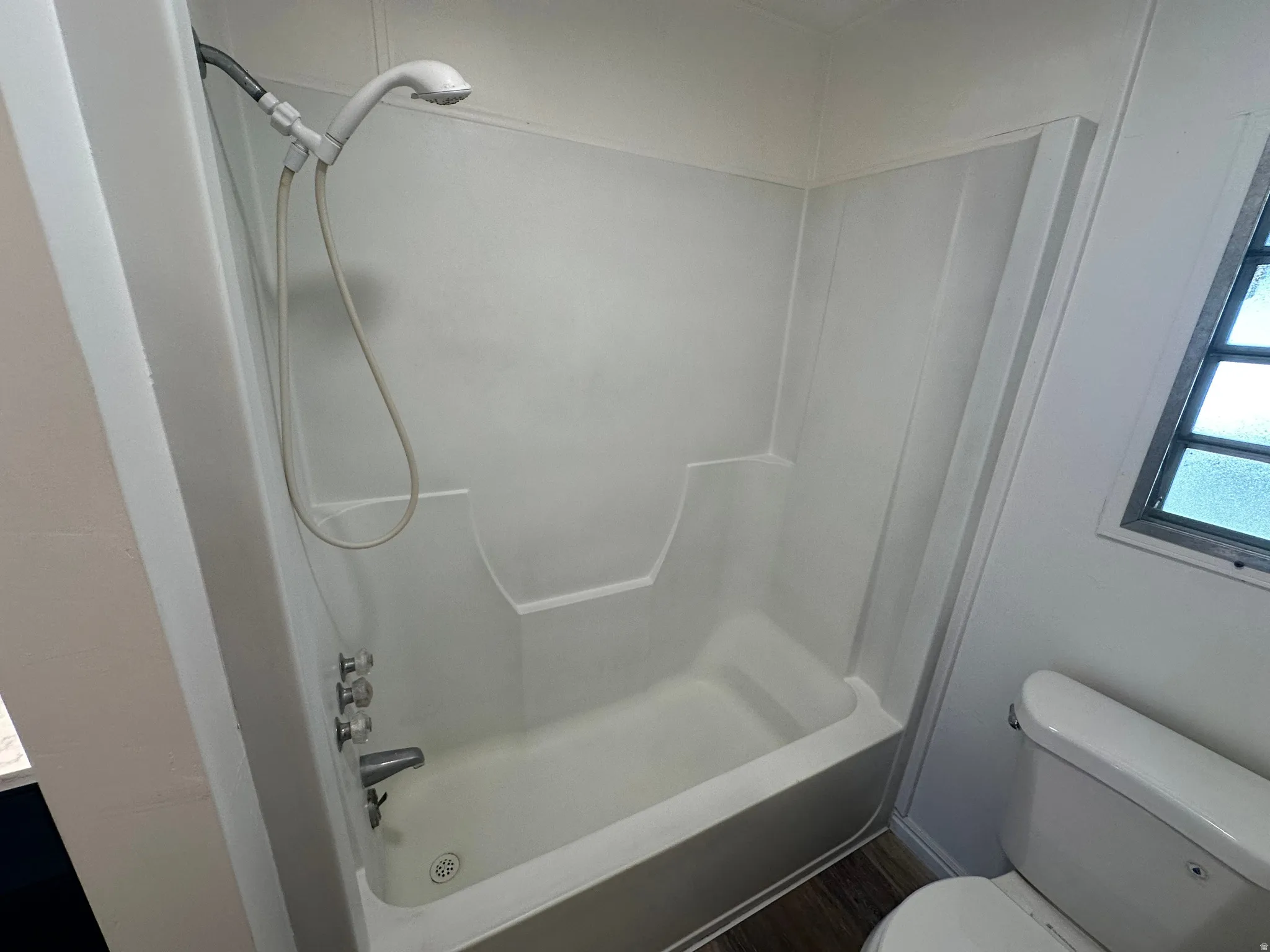 White bathtub and shower combination unit featuring a handheld showerhead, chrome fixtures, and a clear glass block window