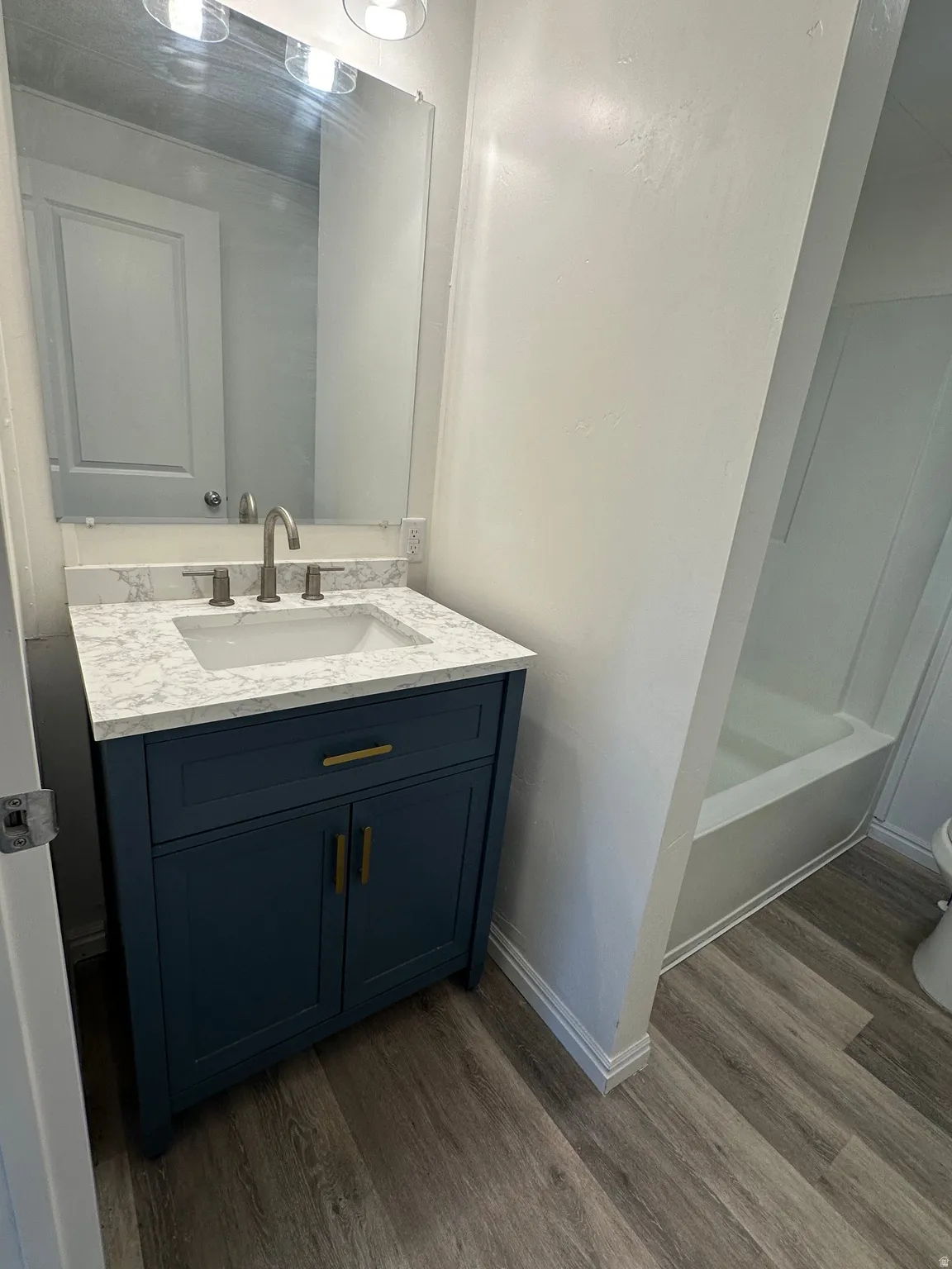 Bathroom featuring a blue vanity with gold-tone hardware, a white countertop with integrated sink, and a large wall-mounted mirror