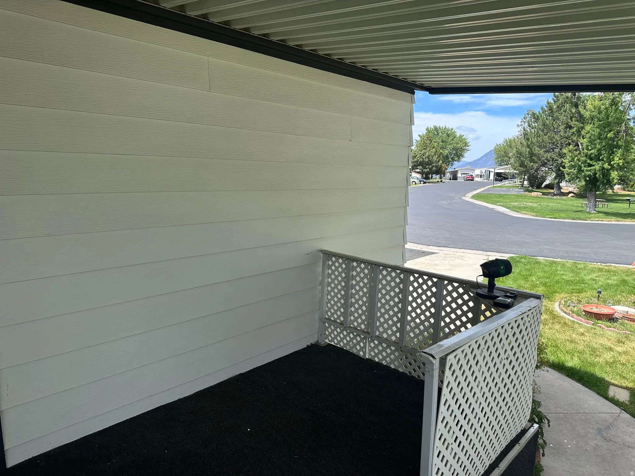 Covered exterior entrance featuring white horizontal siding, a white lattice railing, and a black ground surface
