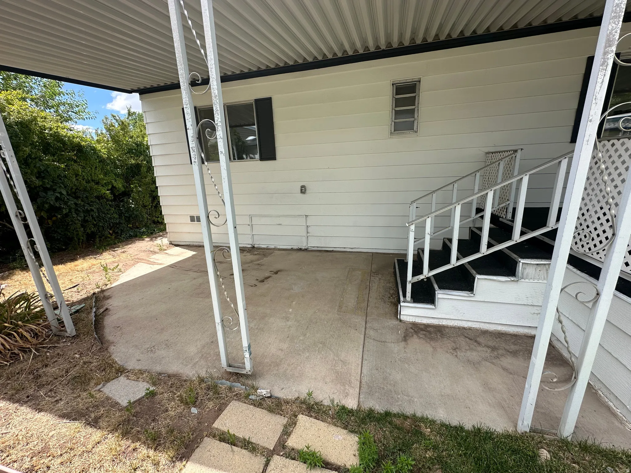 Covered concrete patio area with white siding and an exterior staircase featuring black treads