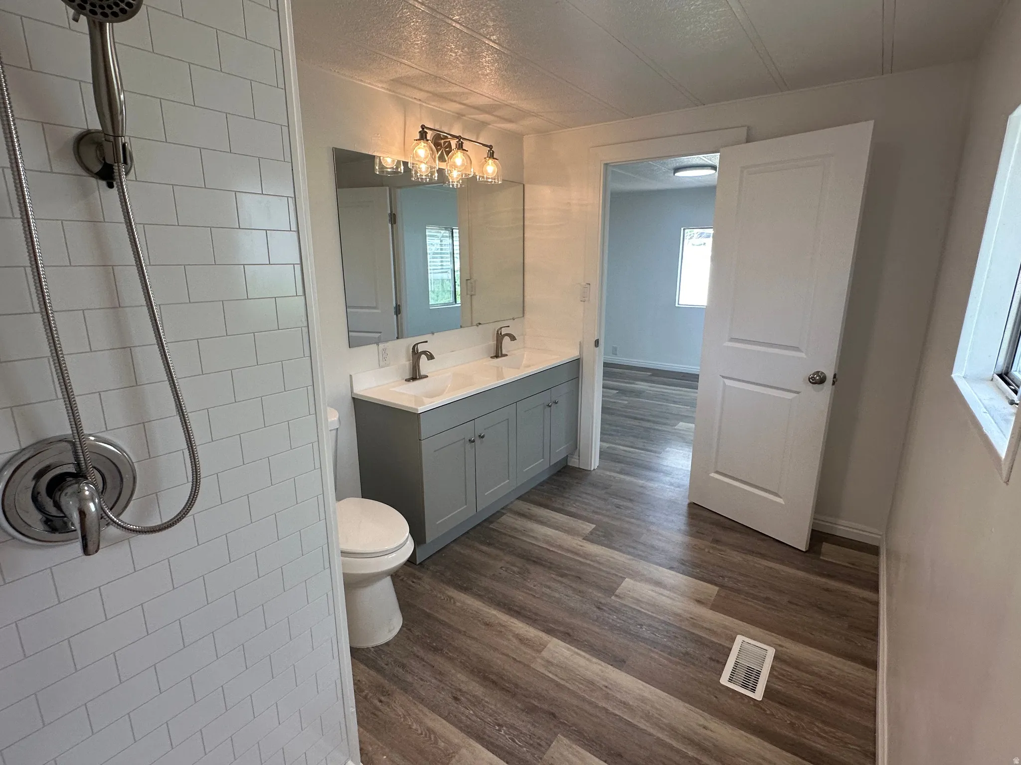Bathroom featuring a dual vanity with a light gray cabinet base, wood-finish flooring, and subway tile shower surround