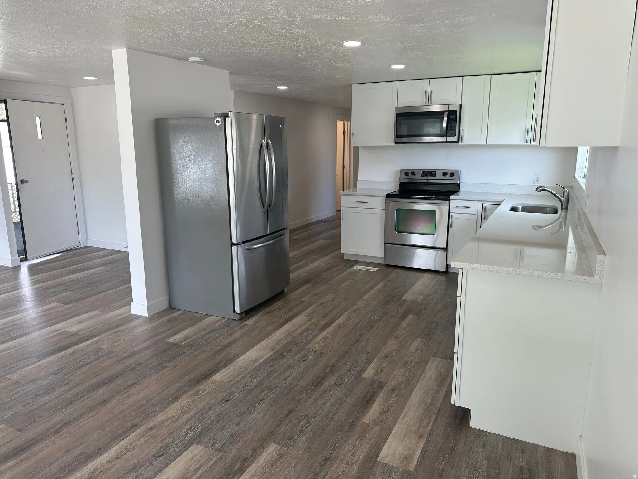 Kitchen featuring wood-finish flooring, white cabinetry, light-colored countertops, and stainless steel appliances including a refrigerator, range, and microwave
