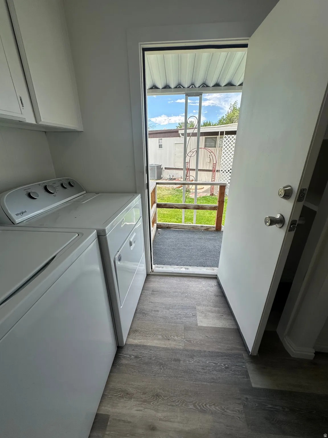 Laundry area with wood-finish flooring, white cabinetry, and access to an exterior landing with a security screen door