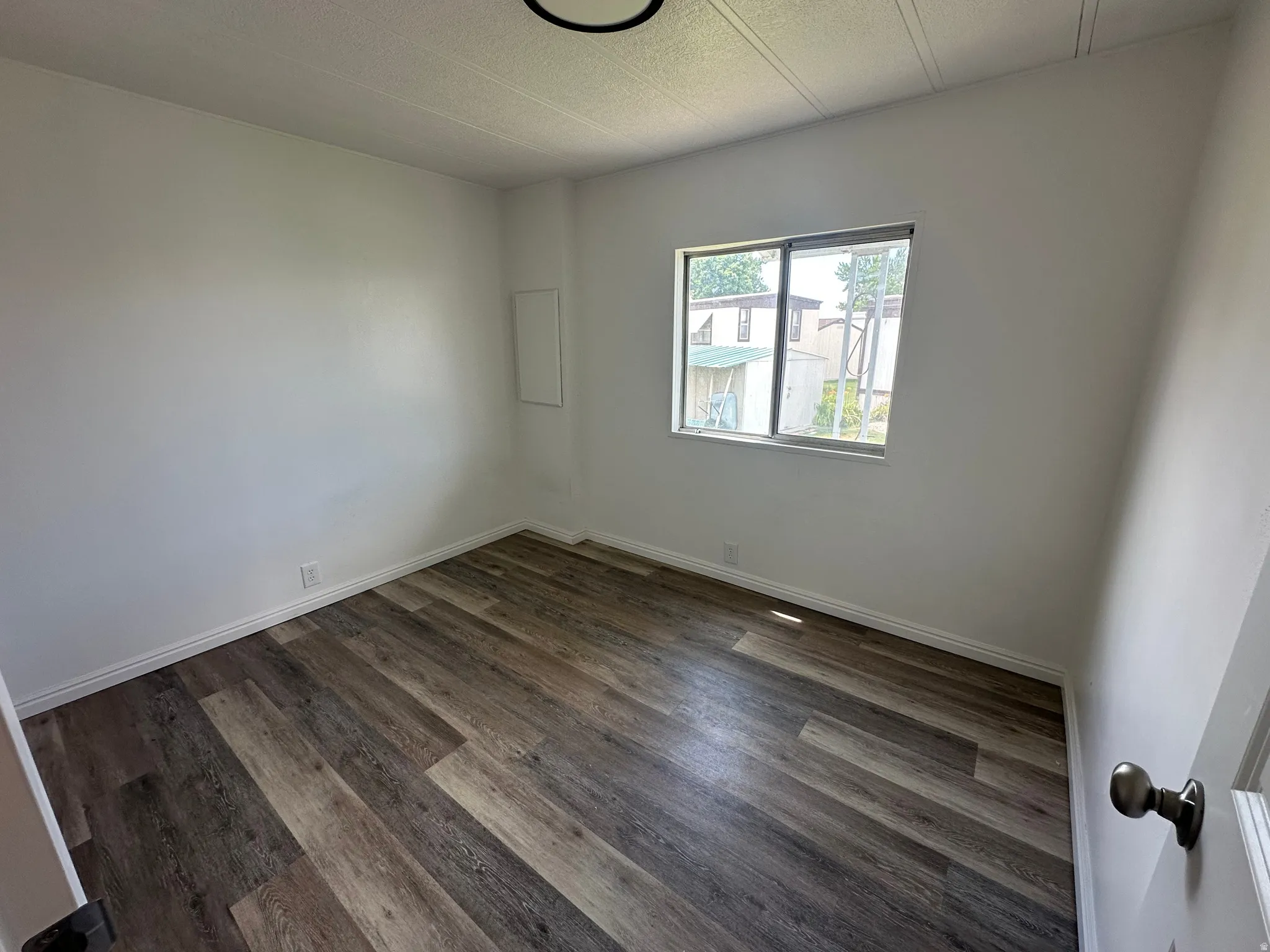 Room featuring wood-finish flooring, white walls, and a single window with a silver frame