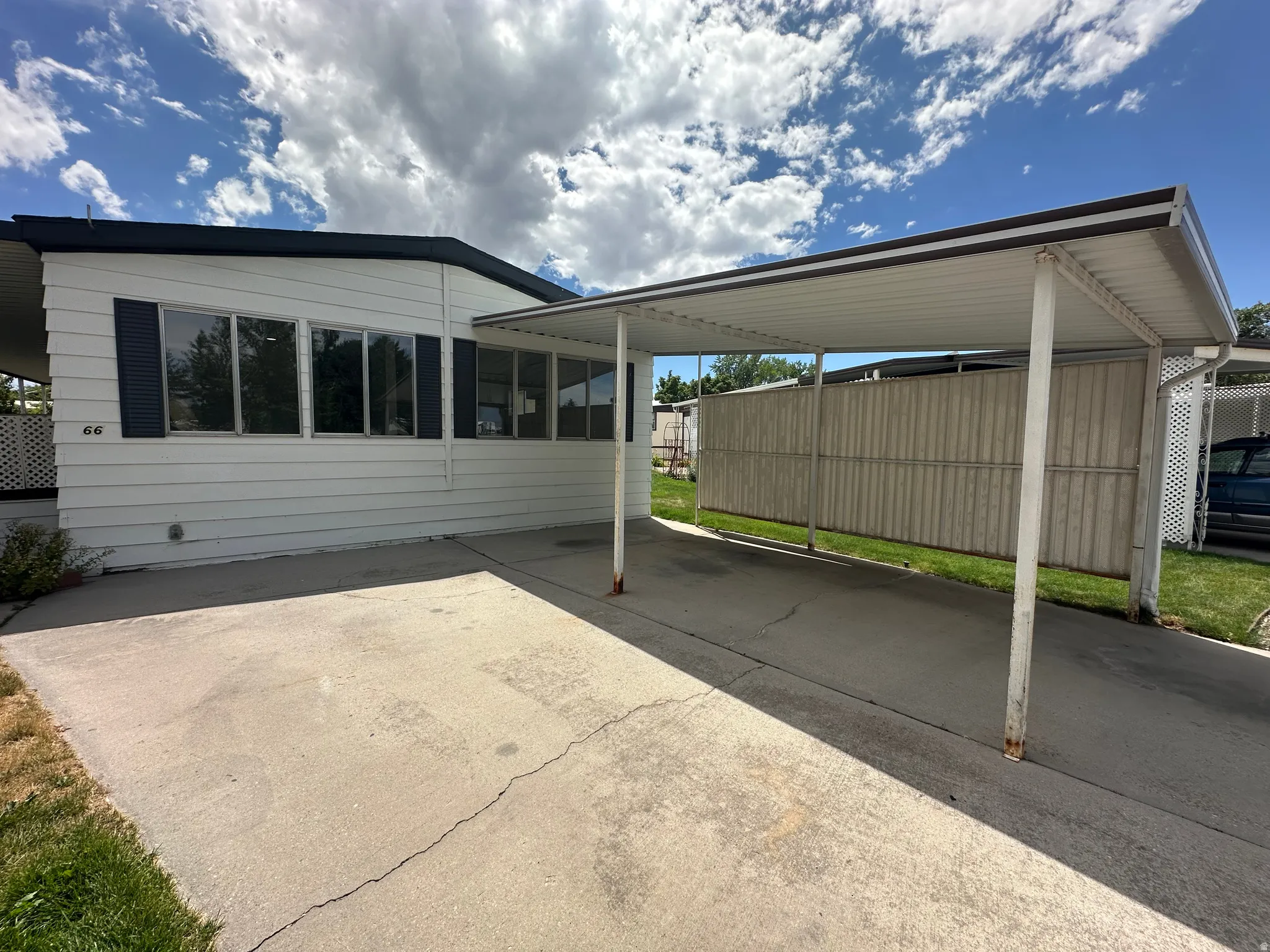 White siding exterior with dark shutters, featuring a covered carport and concrete driveway