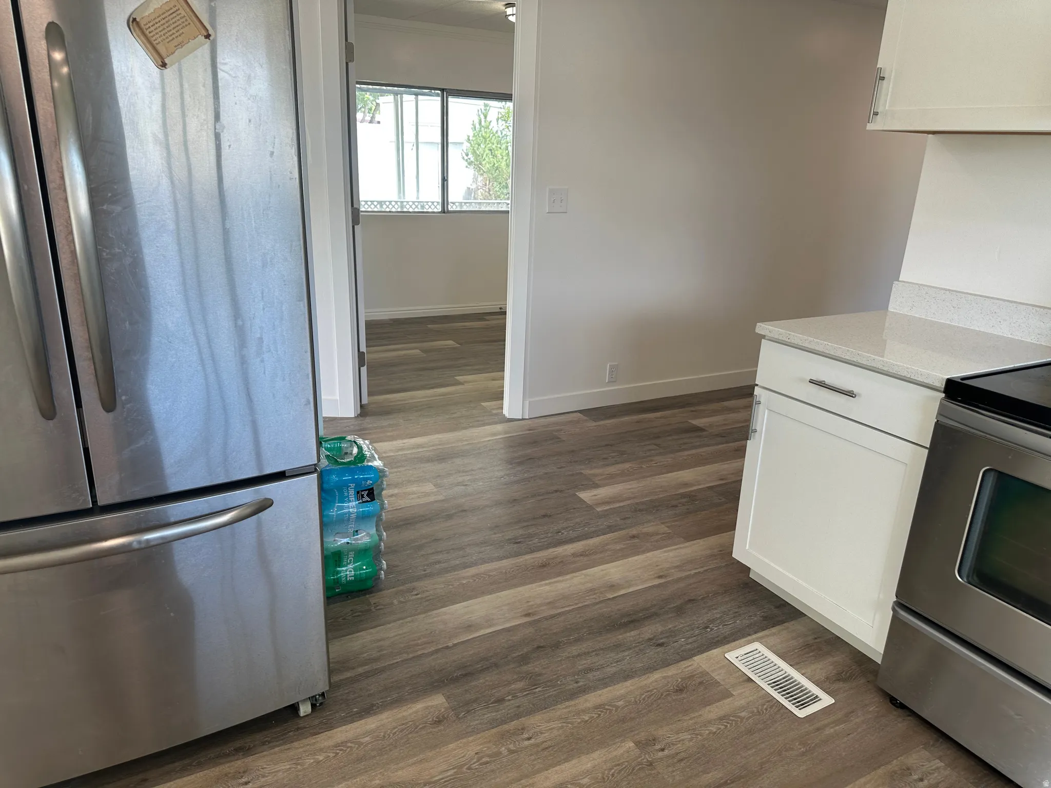 Modern kitchen area featuring stainless steel appliances, white cabinetry with silver hardware, and a light-toned countertop