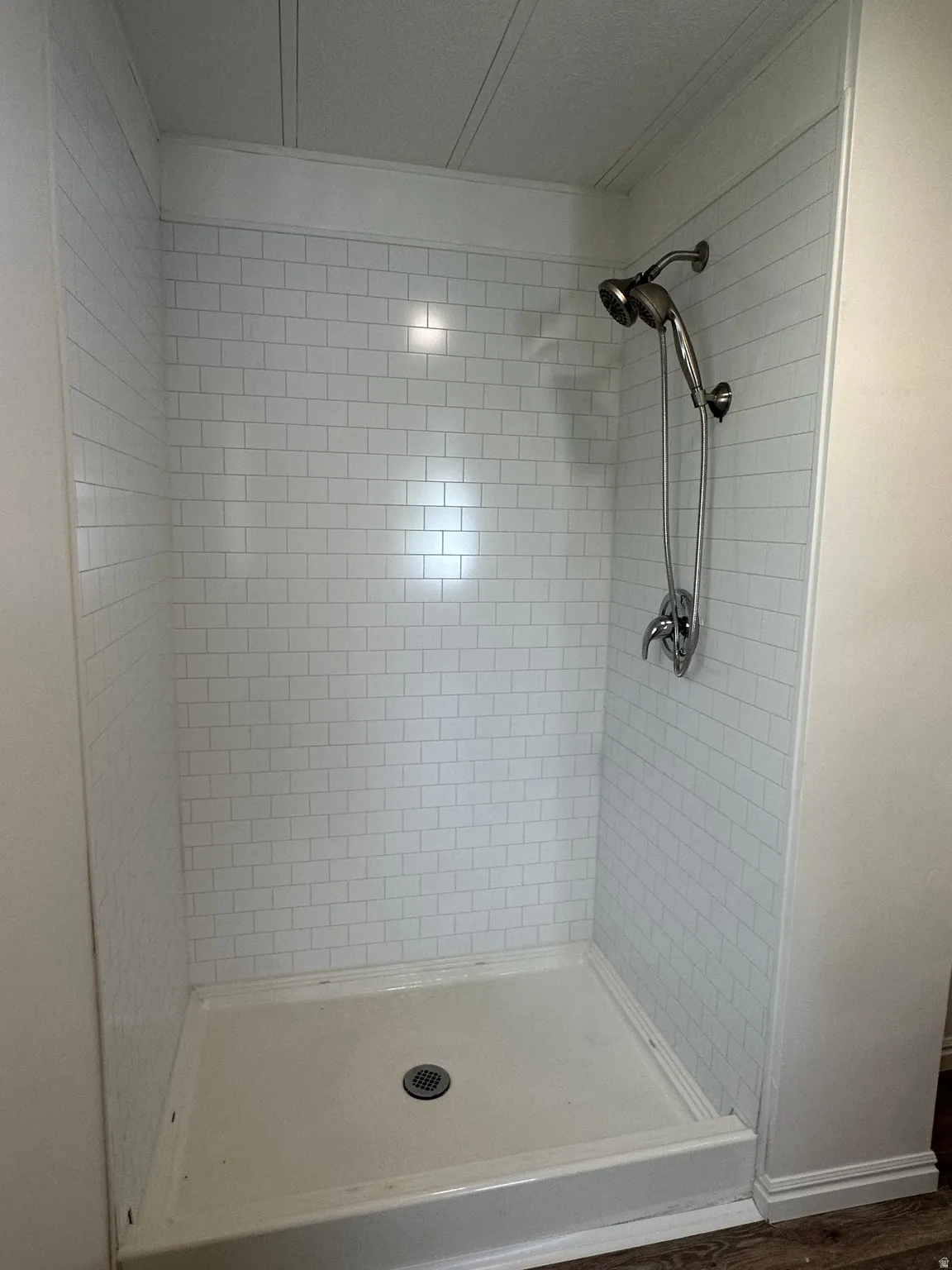 Walk-in shower featuring white subway tile surround, integrated shower base, brushed nickel fixtures, and a ceiling with beadboard paneling
