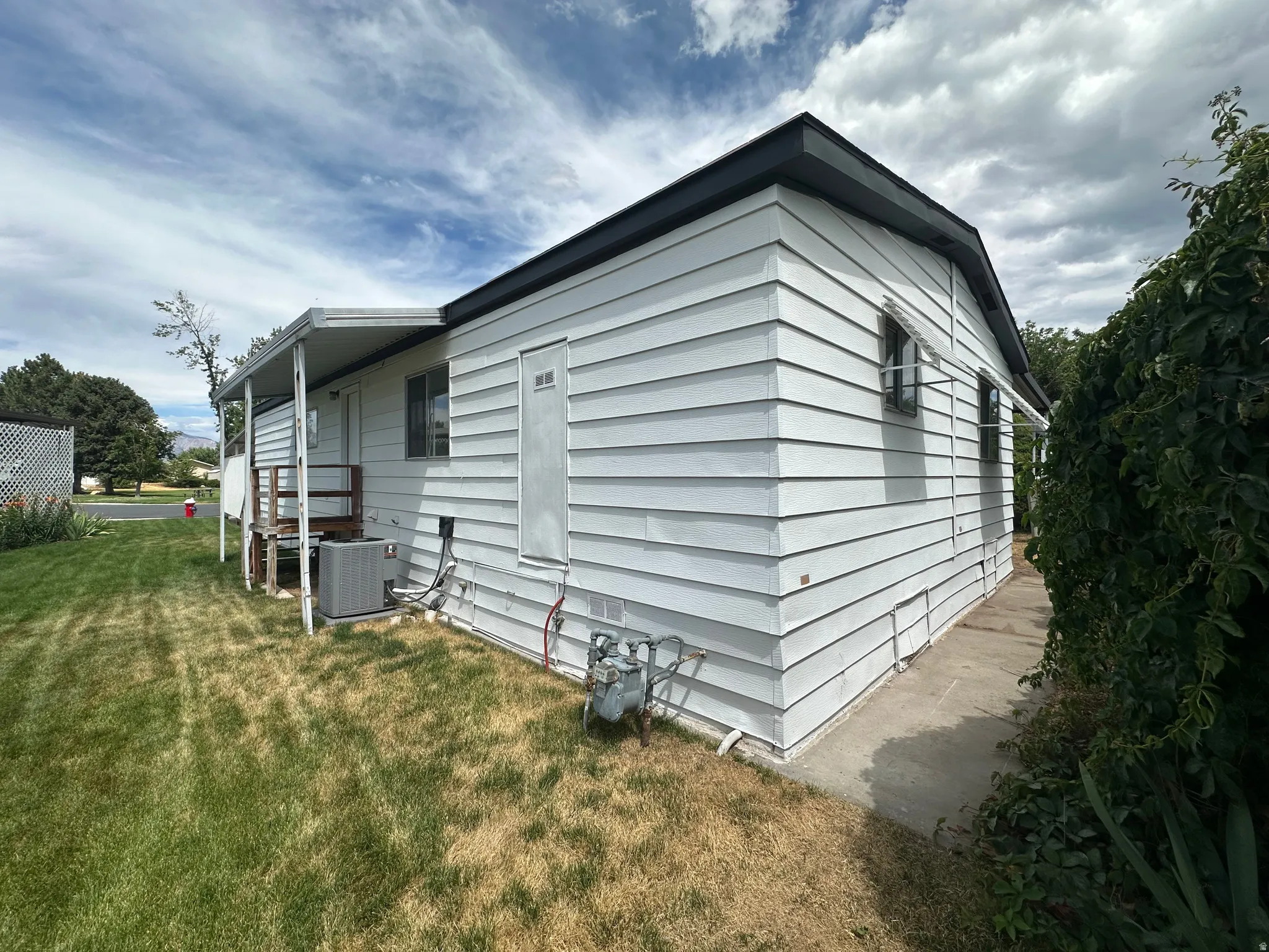 White horizontal siding with dark trim, featuring a side entry with a covered porch and an air conditioning unit