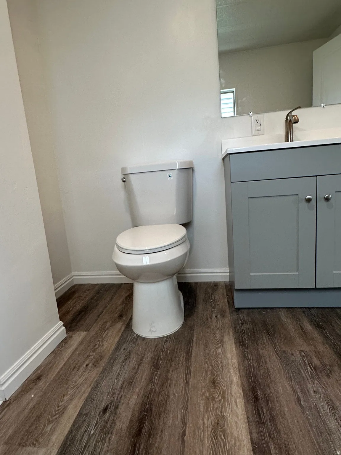 Bathroom featuring a modern toilet, wood-finish flooring, a contemporary vanity with a white countertop, and a wall-mounted mirror
