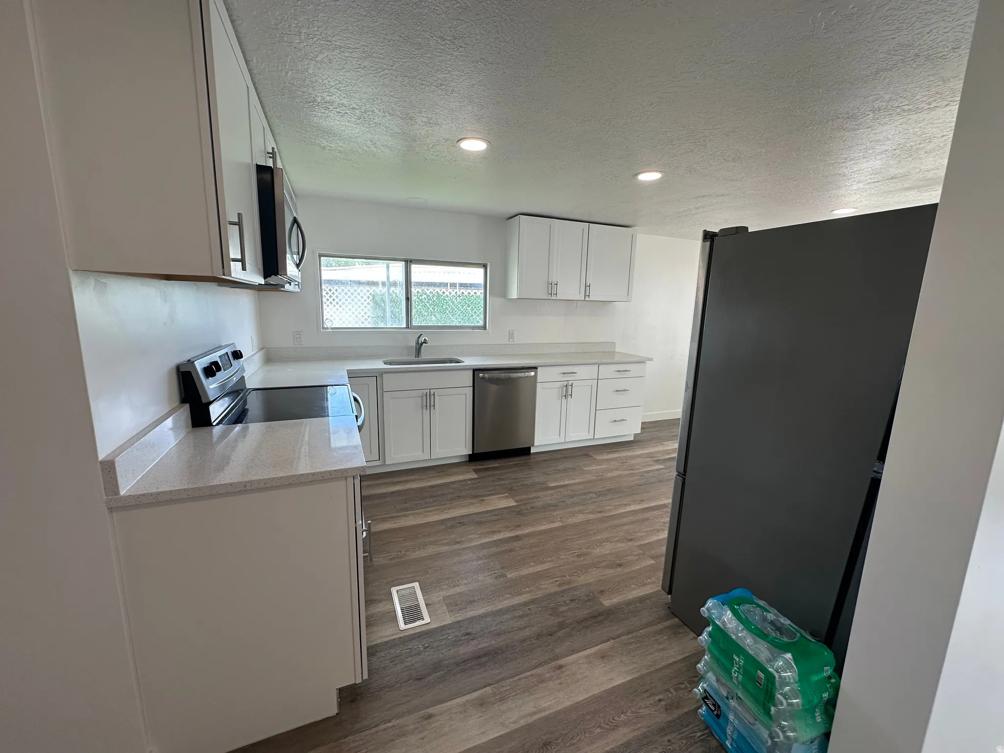Modern kitchen featuring white cabinetry, light-toned countertops, wood-finish flooring, recessed lighting, and stainless steel appliances