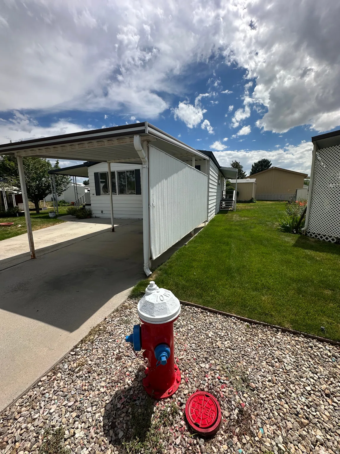 White exterior siding with a covered carport, concrete driveway, and a manicured lawn