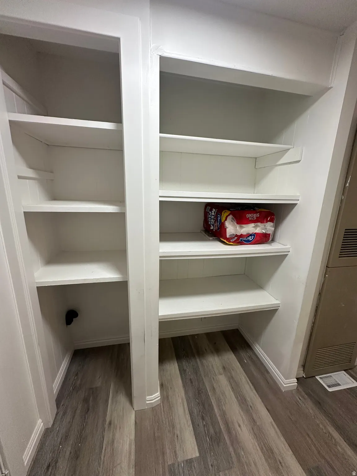 Built-in shelving units featuring multiple white shelves and grey wood-finish flooring