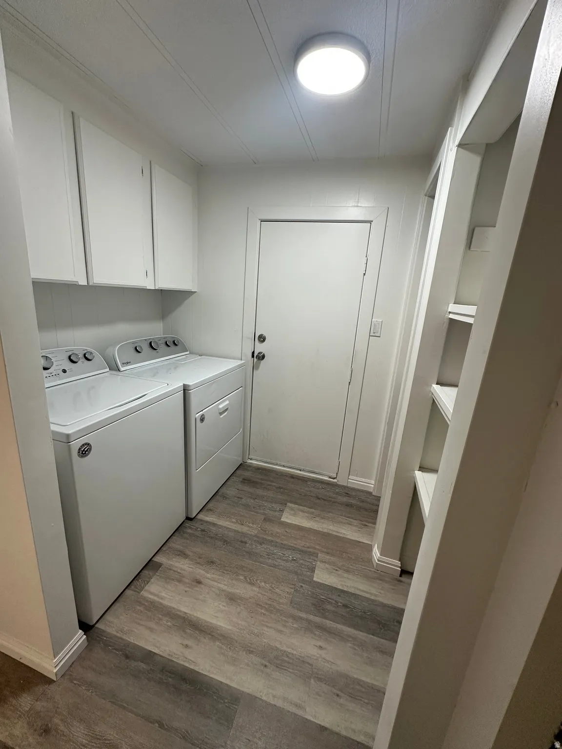 Laundry room featuring wood-finish flooring, white cabinetry, overhead lighting, and built-in shelving