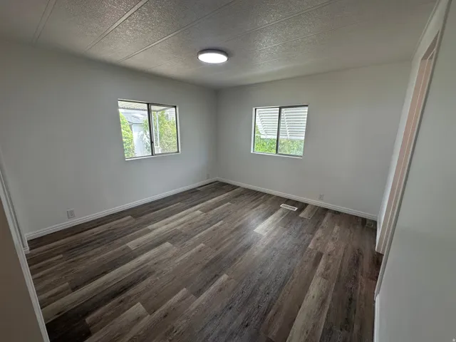 Room featuring wood-finish flooring, white walls, and two windows