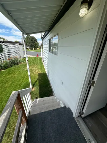 Covered outdoor entry with wood steps and railing, white horizontal siding, and a small window