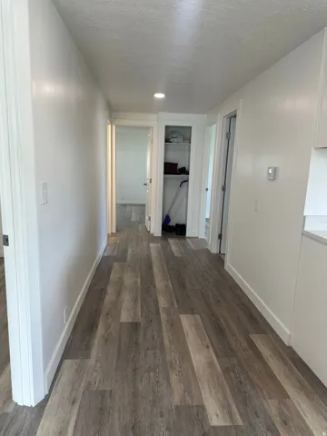 Hallway featuring wood-finish flooring, white painted walls, recessed lighting, and a built-in linen closet with shelving