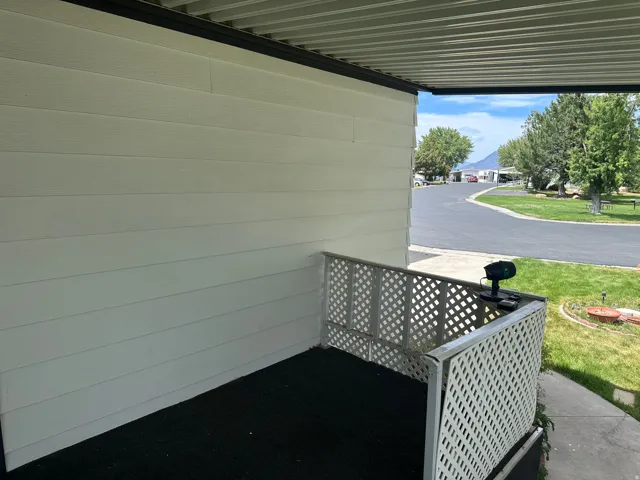 Covered exterior entrance featuring white horizontal siding, a white lattice railing, and a black ground surface