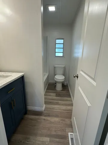 Bathroom featuring a dark blue vanity with gold-tone hardware, a white countertop, and wood-finish flooring
