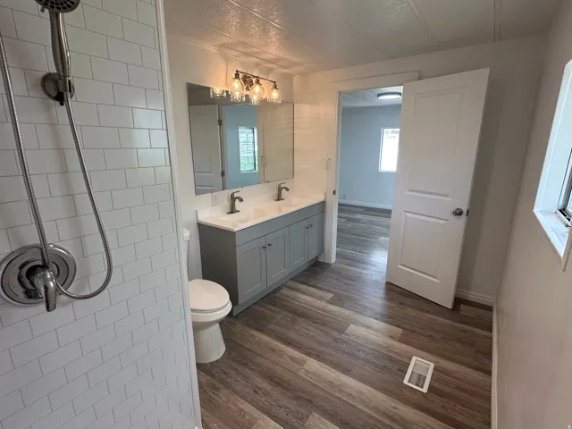 Bathroom featuring a dual vanity with a light gray cabinet base, wood-finish flooring, and subway tile shower surround