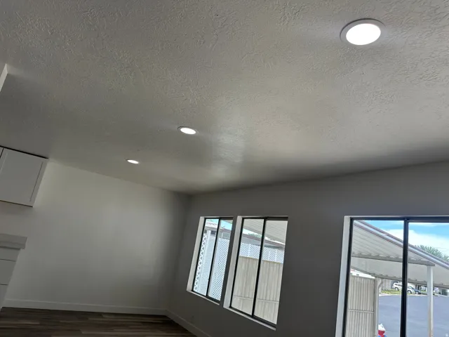 Recessed lighting illuminating a textured ceiling, complemented by multiple windows with dark framing