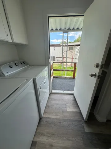 Laundry area with wood-finish flooring, white cabinetry, and access to an exterior landing with a security screen door