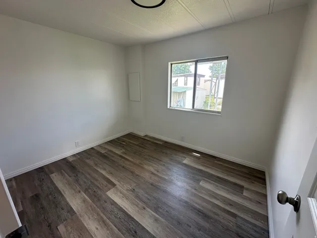 Room featuring wood-finish flooring, white walls, and a single window with a silver frame