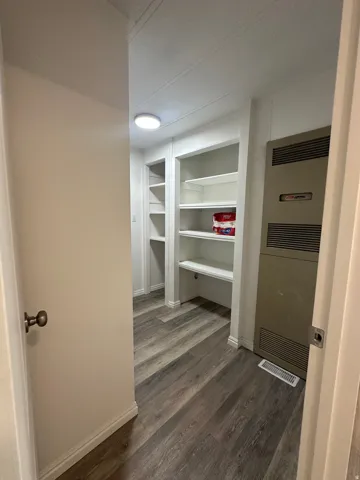 Hallway featuring wood-finish flooring, built-in shelving, white baseboards, and a wall-mounted heating unit