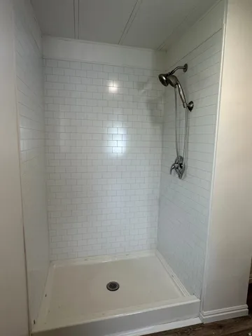 Walk-in shower featuring white subway tile surround, integrated shower base, brushed nickel fixtures, and a ceiling with beadboard paneling