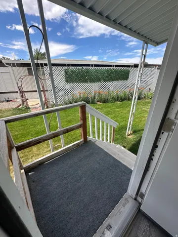 Covered porch area with wood railings, leading to a vibrant green lawn